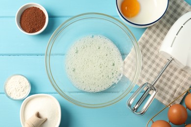 Photo of Making whipped cream. Bowl, hand mixer and ingredients on light blue wooden table, flat lay