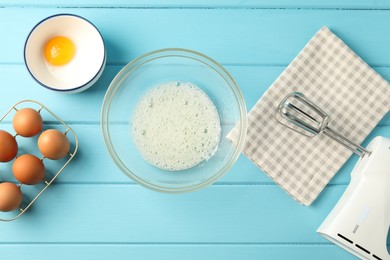 Photo of Making whipped cream. Bowl, hand mixer and ingredients on light blue wooden table, flat lay