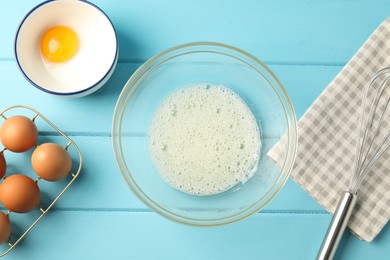 Photo of Making whipped cream. Bowl, whisk and ingredients on light blue wooden table, flat lay