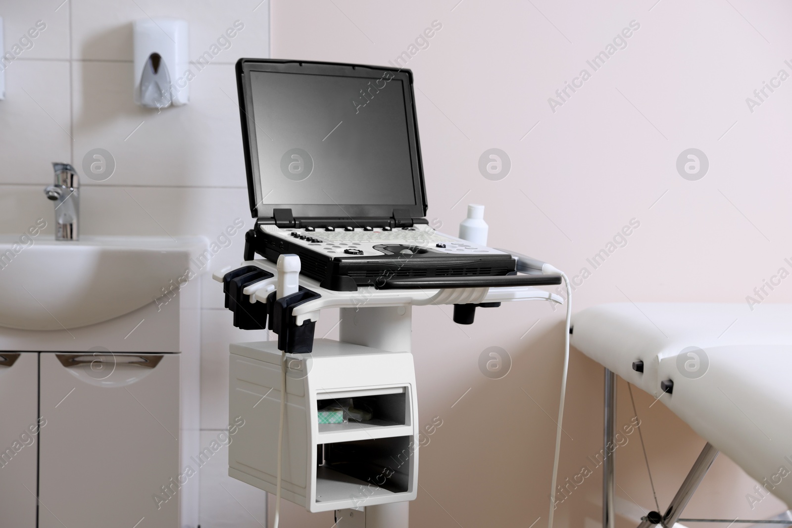 Modern ultrasound machine, sink and examination bed in clinic Photo of Modern ultrasound machine, sink and examination bed in clinic