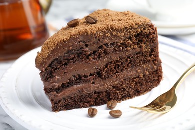 Photo of Piece of delicious chocolate cake with coffee beans and fork on white table, closeup