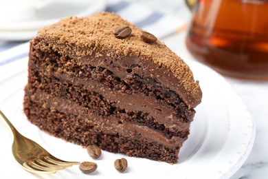 Photo of Piece of delicious chocolate cake with coffee beans and fork on white table, closeup