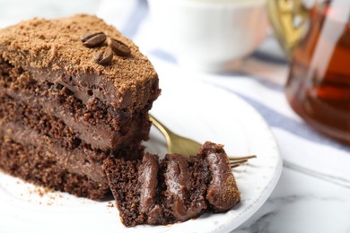 Photo of Piece of delicious chocolate cake with coffee beans and fork on white marble table, closeup