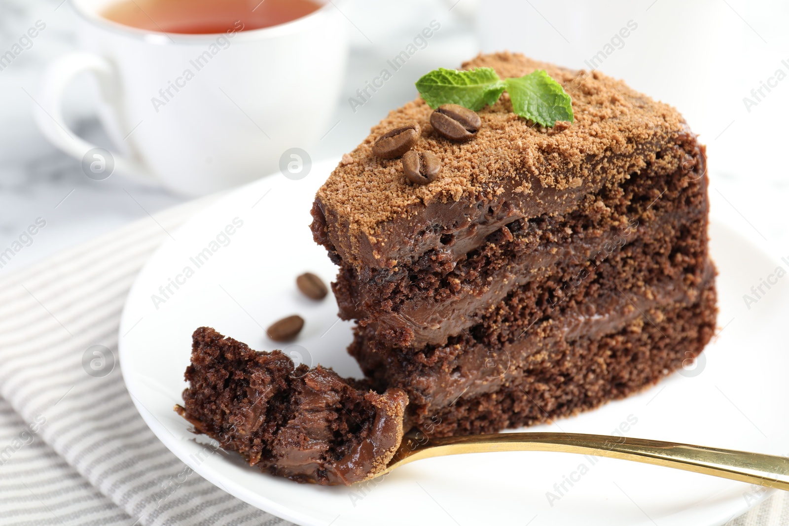 Photo of Piece of delicious chocolate cake with coffee beans, mint and fork on light table, closeup