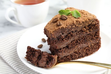 Photo of Piece of delicious chocolate cake with coffee beans, mint and fork on light table, closeup