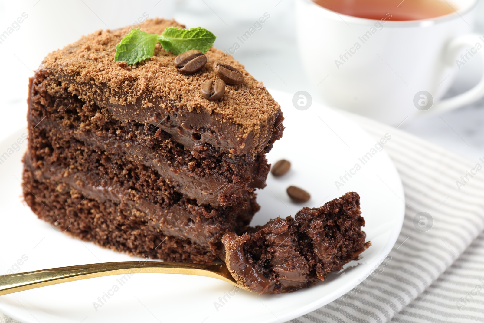Piece of delicious chocolate cake with coffee beans, mint and fork on light table, closeup Photo of Piece of delicious chocolate cake with coffee beans, mint and fork on light table, closeup