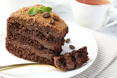 Photo of Piece of delicious chocolate cake with coffee beans, mint and fork on light table, closeup