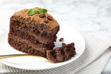 Photo of Piece of delicious chocolate cake with coffee beans, mint and fork on light table, closeup