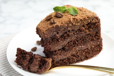 Photo of Piece of delicious chocolate cake with coffee beans, mint and fork on light table, closeup