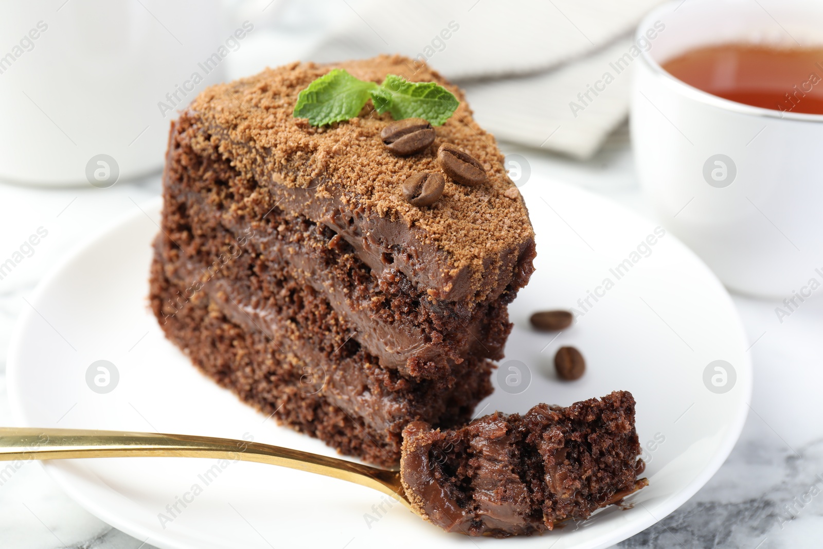 Piece of delicious chocolate cake with coffee beans, mint and fork on white marble table, closeup Photo of Piece of delicious chocolate cake with coffee beans, mint and fork on white marble table, closeup