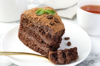 Photo of Piece of delicious chocolate cake with coffee beans, mint and fork on white marble table, closeup