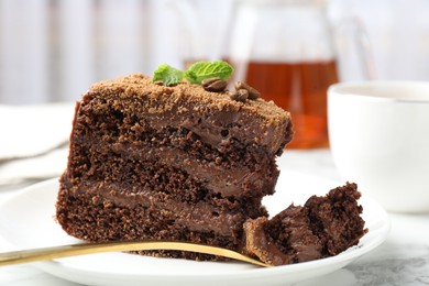 Photo of Piece of delicious chocolate cake with coffee beans, mint and fork on white marble table, closeup