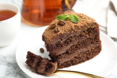 Photo of Piece of delicious chocolate cake with coffee beans, mint and fork on white marble table, closeup