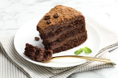 Photo of Piece of delicious chocolate cake with coffee beans, mint and fork on light table, closeup