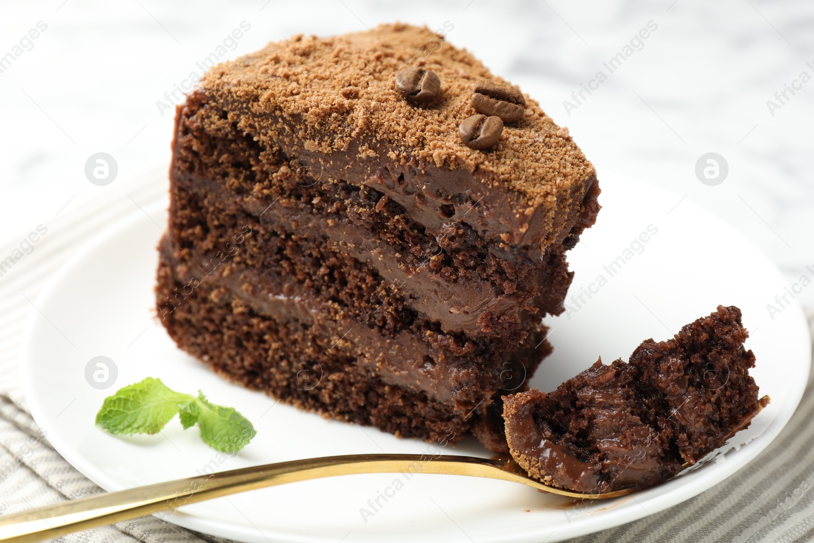 Photo of Piece of delicious chocolate cake with coffee beans, mint and fork on light table, closeup