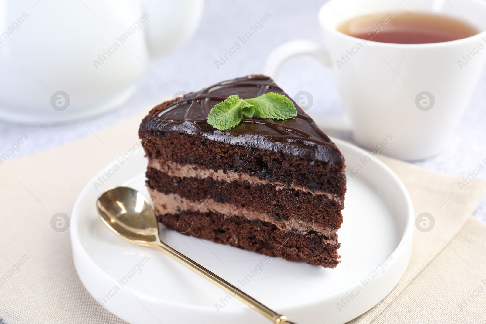 Photo of Piece of delicious chocolate cake with mint and spoon on light table, closeup