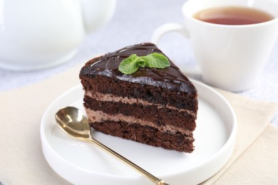 Photo of Piece of delicious chocolate cake with mint and spoon on light table, closeup
