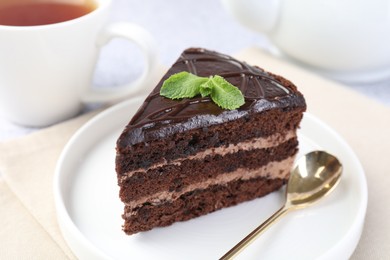 Photo of Piece of delicious chocolate cake with mint and spoon on light table, closeup