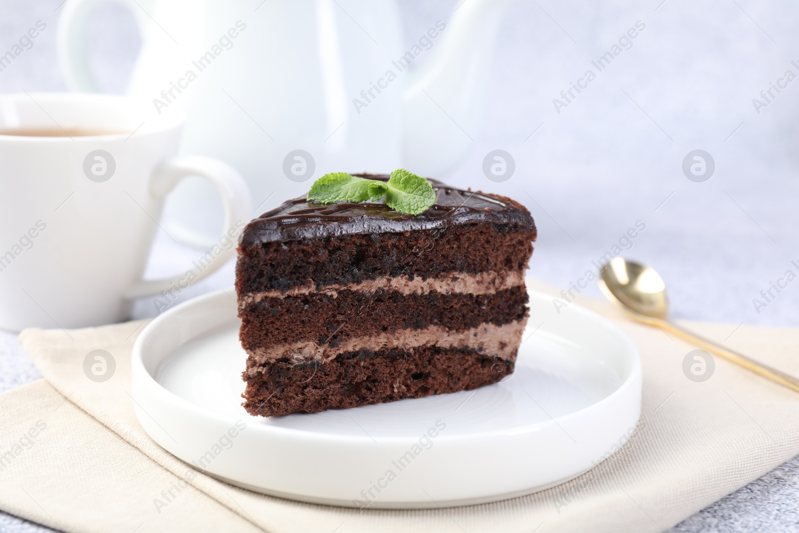 Piece of delicious chocolate cake with mint and spoon on grey table, closeup Photo of Piece of delicious chocolate cake with mint and spoon on grey table, closeup