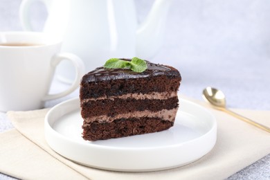 Photo of Piece of delicious chocolate cake with mint and spoon on grey table, closeup