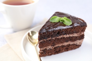 Photo of Piece of delicious chocolate cake, mint and spoon on light table, closeup