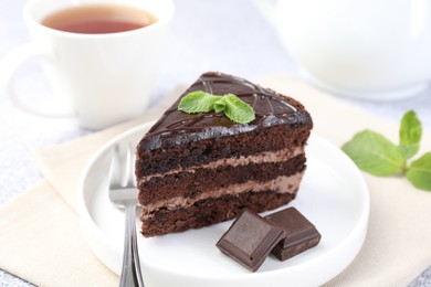 Photo of Piece of delicious chocolate cake, mint and fork on light table, closeup