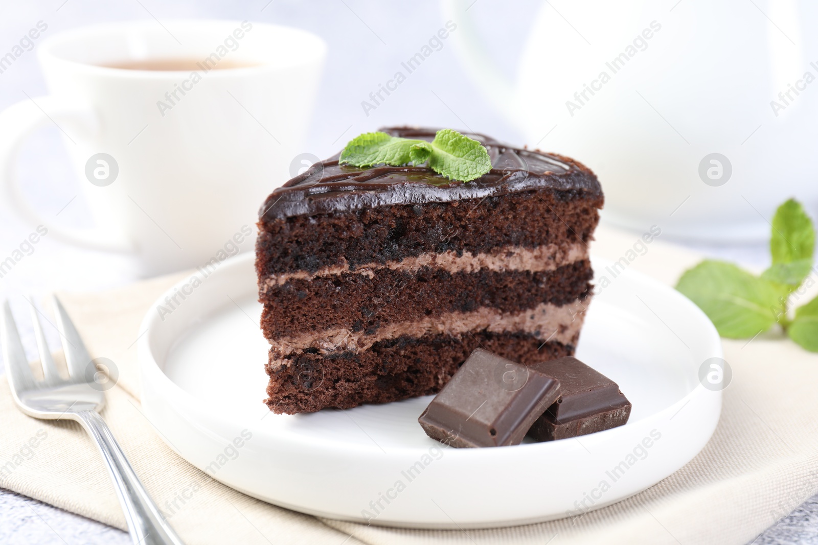 Photo of Piece of delicious cake, mint, chocolate and fork on light table, closeup