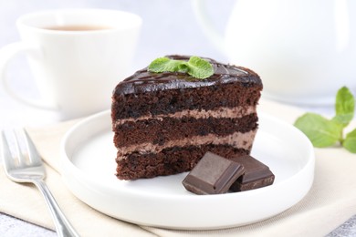 Photo of Piece of delicious cake, mint, chocolate and fork on light table, closeup