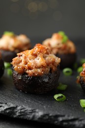 Photo of Tasty stuffed mushrooms served on black table against blurred background, closeup
