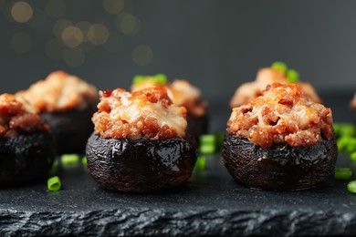 Photo of Tasty stuffed mushrooms served on black table against blurred background, closeup