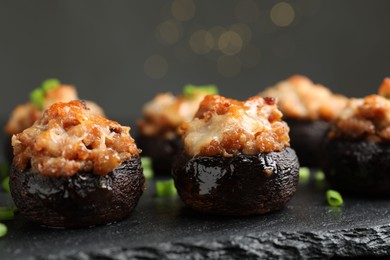 Photo of Tasty stuffed mushrooms served on black table against blurred background, closeup