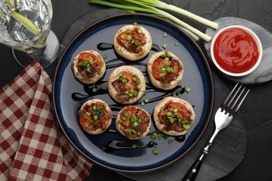 Photo of Tasty stuffed mushrooms served on black table, flat lay