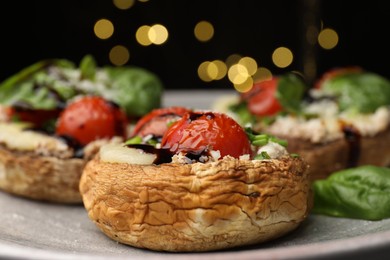 Photo of Tasty stuffed mushrooms served on black table against blurred background, closeup. Bokeh effect
