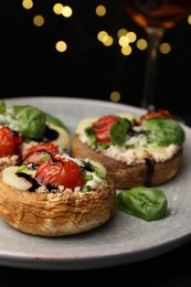 Photo of Tasty stuffed mushrooms served on black table against blurred background, closeup. Bokeh effect