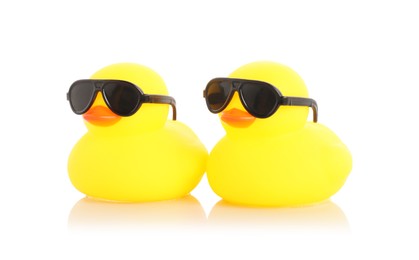 Photo of Cute rubber ducks in sunglasses on mirror surface against white background