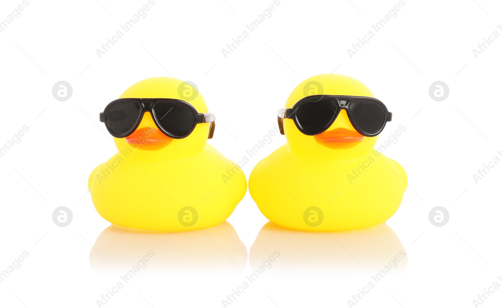 Cute rubber ducks in sunglasses on mirror surface against white background Photo of Cute rubber ducks in sunglasses on mirror surface against white background