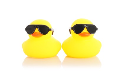 Photo of Cute rubber ducks in sunglasses on mirror surface against white background