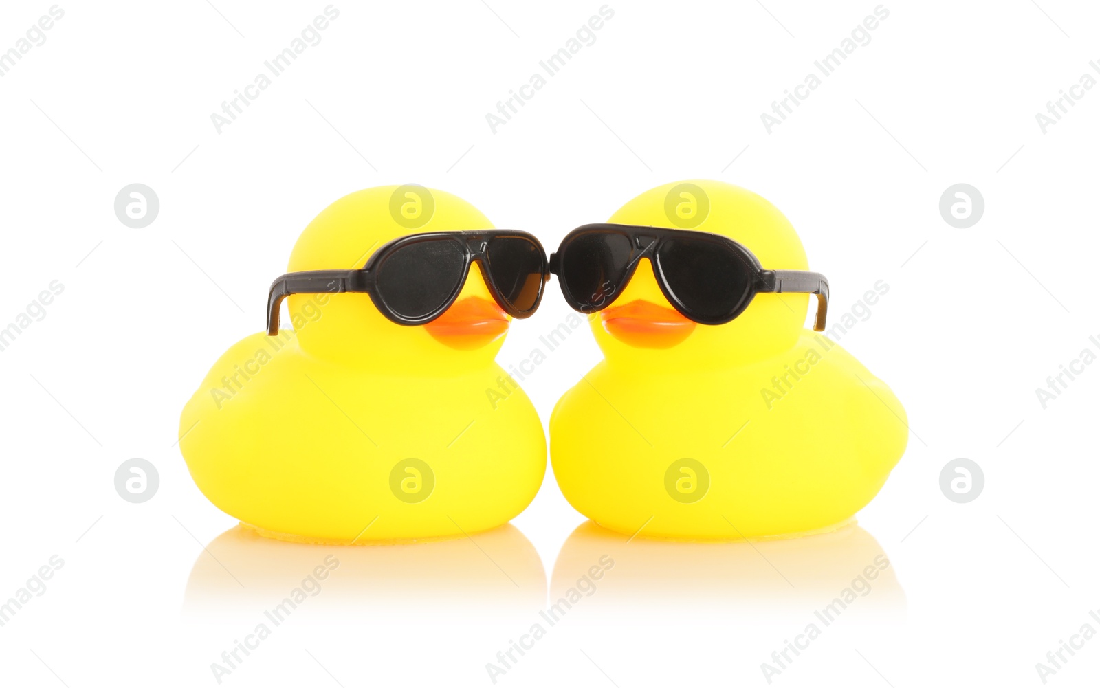 Cute rubber ducks in sunglasses on mirror surface against white background Photo of Cute rubber ducks in sunglasses on mirror surface against white background