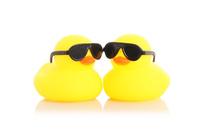 Photo of Cute rubber ducks in sunglasses on mirror surface against white background