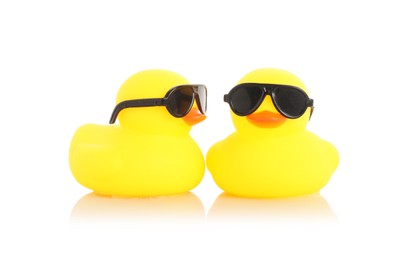 Photo of Cute rubber ducks in sunglasses on mirror surface against white background