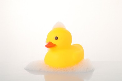 Photo of One cute rubber duck and foam on mirror surface against white background