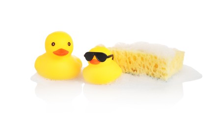 Photo of Cute rubber ducks and sponge with foam on mirror surface against white background