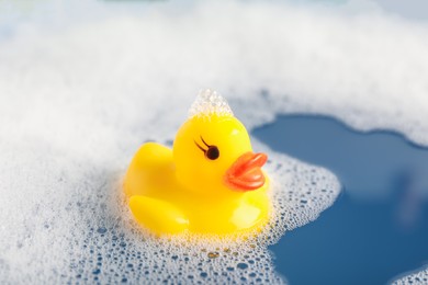 Photo of Cute rubber duck floating in water with bubbles, closeup