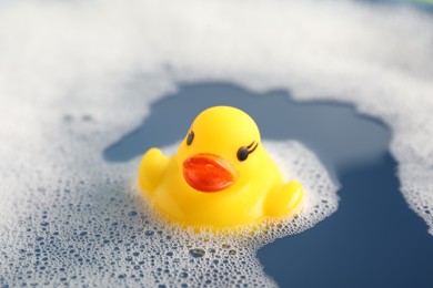 Photo of Cute rubber duck floating in water with bubbles, closeup