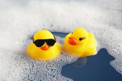 Photo of Cute rubber ducks floating in water with bubbles, closeup