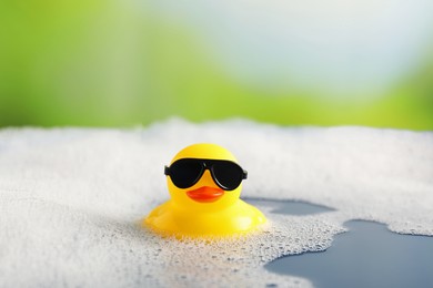 Photo of Cute rubber duck floating in water with bubbles against blurred green background, closeup