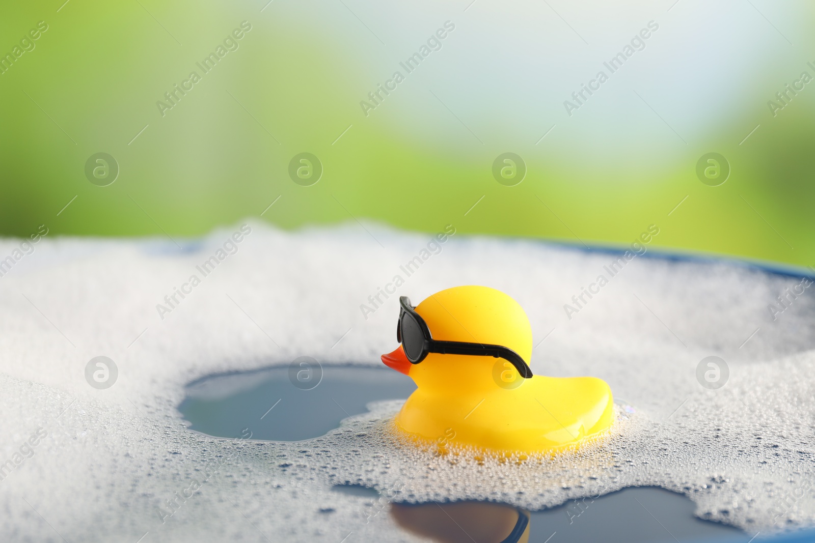 Cute rubber duck floating in water with bubbles against blurred green background, closeup Photo of Cute rubber duck floating in water with bubbles against blurred green background, closeup