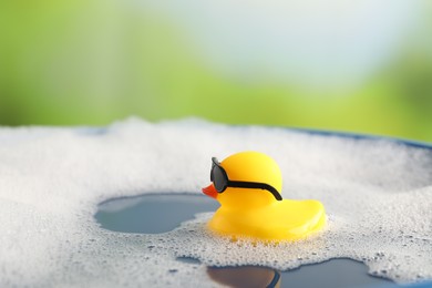Photo of Cute rubber duck floating in water with bubbles against blurred green background, closeup