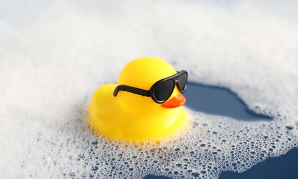 Photo of Cute rubber duck floating in water with bubbles, closeup