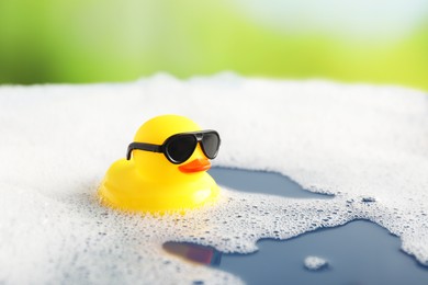 Photo of Cute rubber duck floating in water with bubbles against blurred green background, closeup